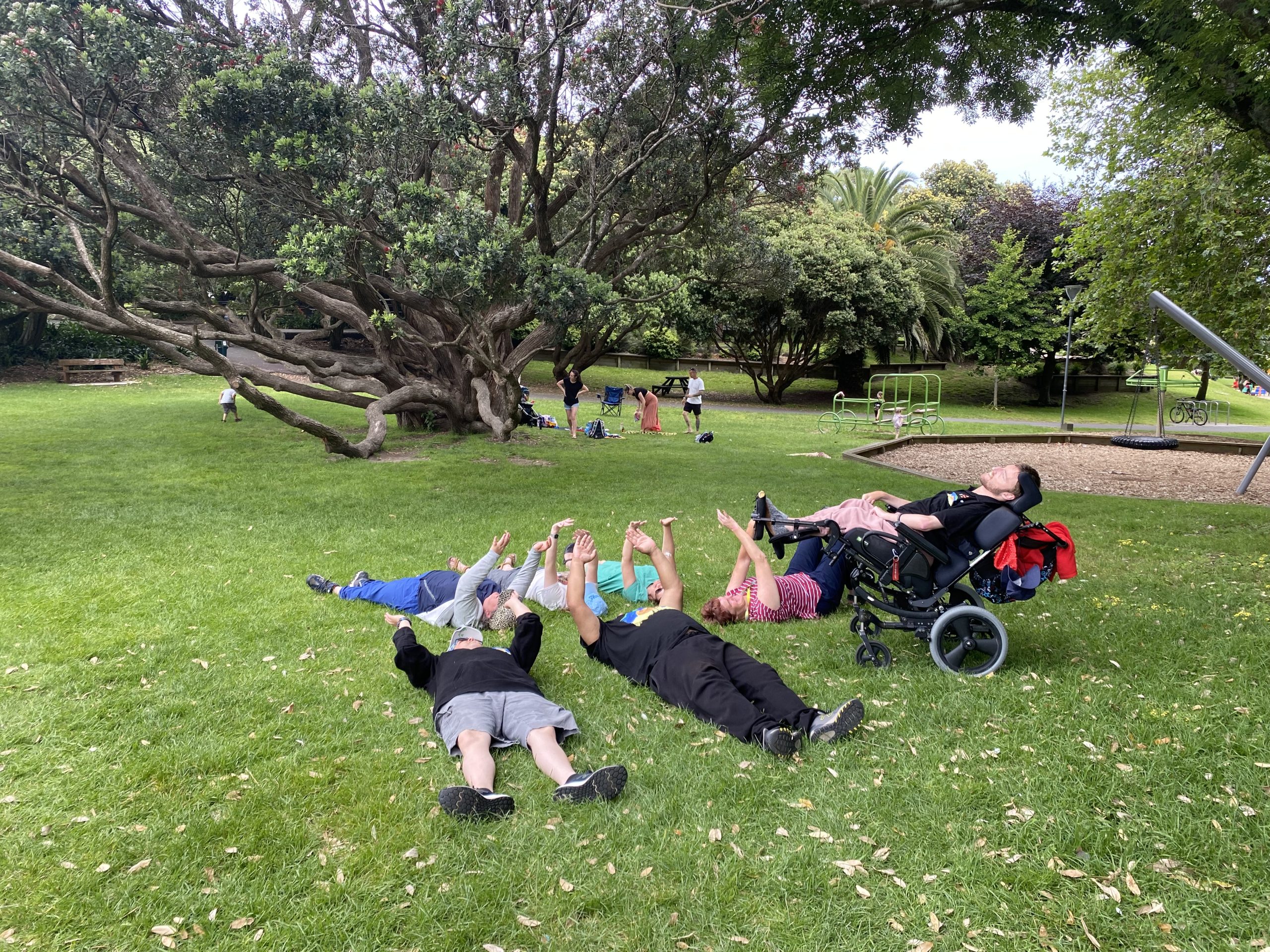 The network group, Kāpiti Kiwis, lying down in the grass in the park with their arms up in the air