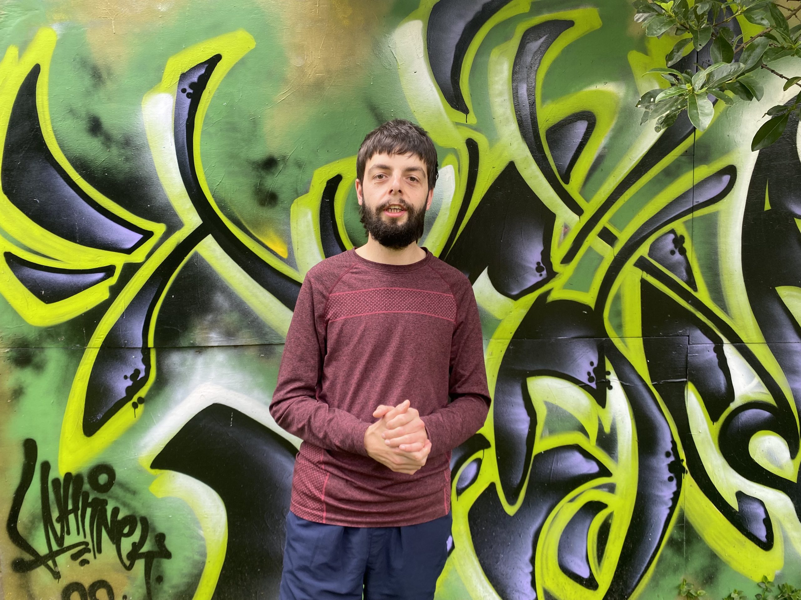 Oliver Gordon Oliver standing with his hands clasped in front of a graffiti wall